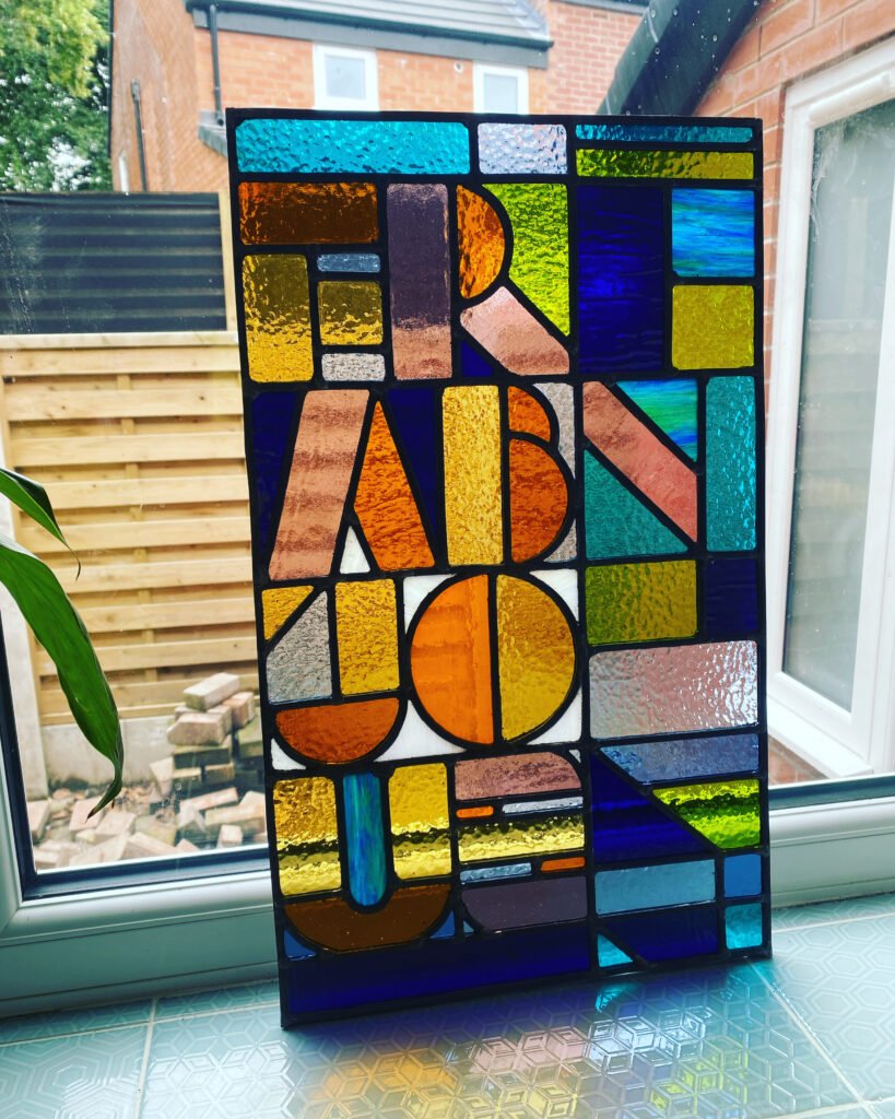 Stained glass window that reads the word FRABJOUS (a made up Alice in Wonderland word meaning joyful)