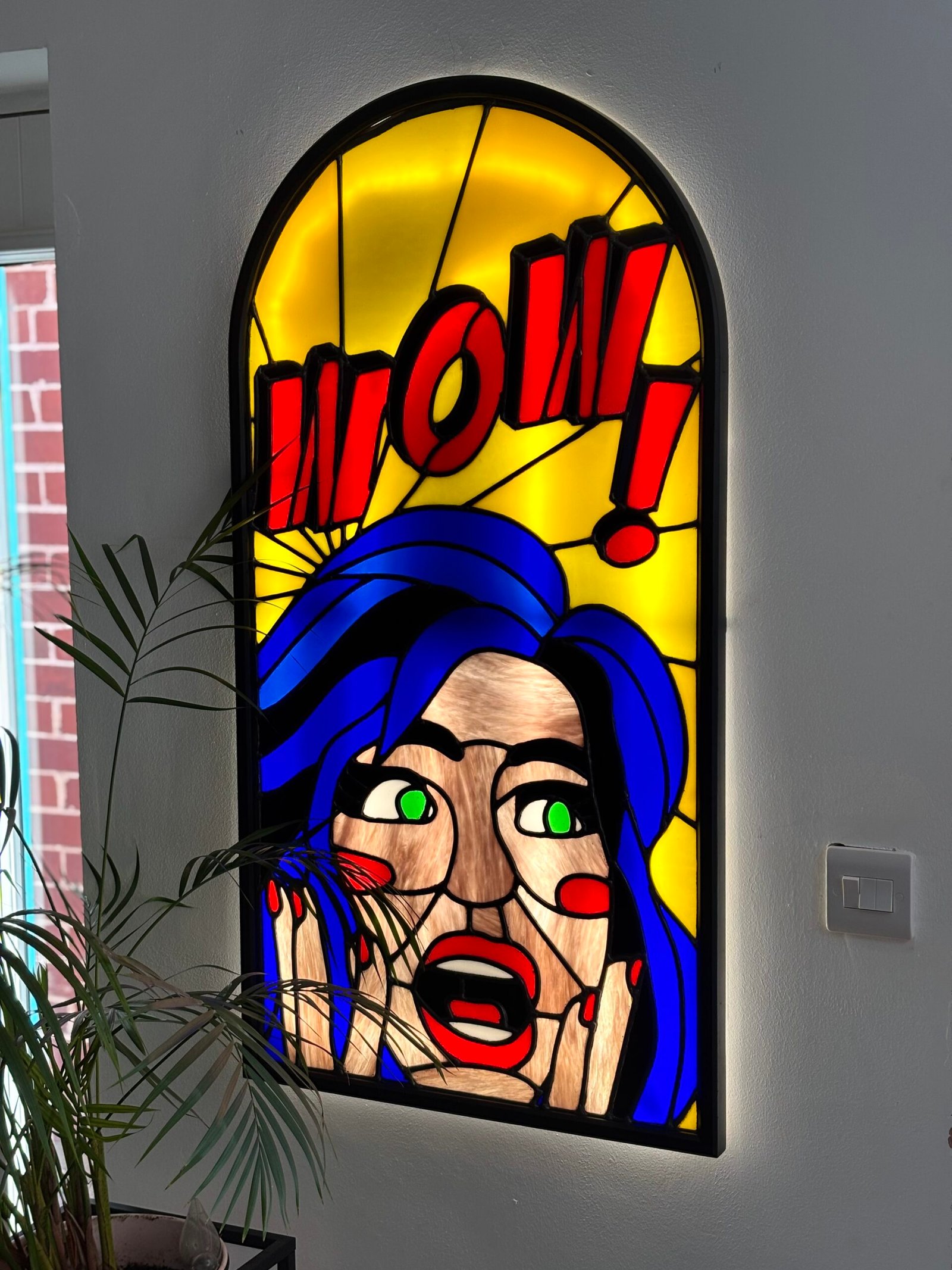 Stained glass light box in a pop art style with a woman with blue hair saying the word WOW!